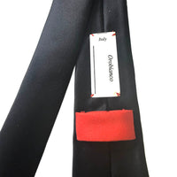 A close-up of a black necktie with a bright red turned-up cuff, showing a white paper tag that reads 'Italy Orbanico'.
