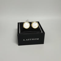 A pair of round gold cufflinks with iridescent mother-of-pearl faces, presented in a black A. Azthom gift box.