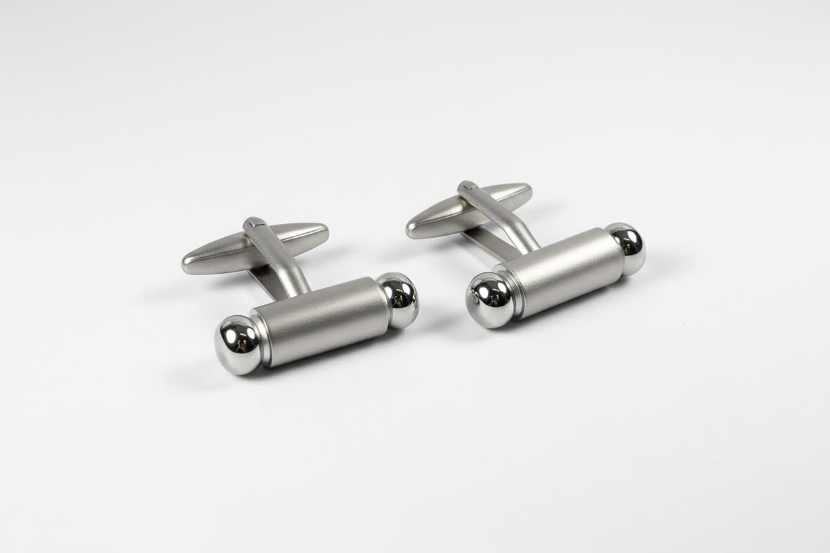 Silver cylindrical cufflinks on a white background