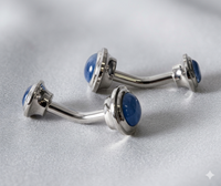 Two silver-toned curved barbell piercings with round blue cateye, displayed on a textured light gray fabric background.